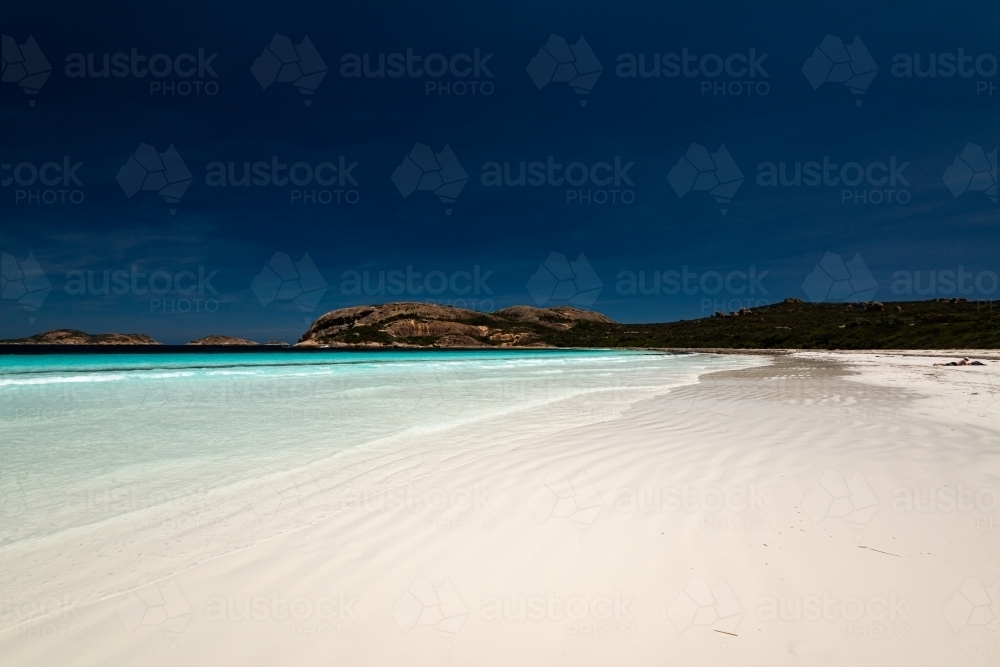Rippling wave patterns on a white sand beach with beautiful clear shore line and deep blue polarised - Australian Stock Image
