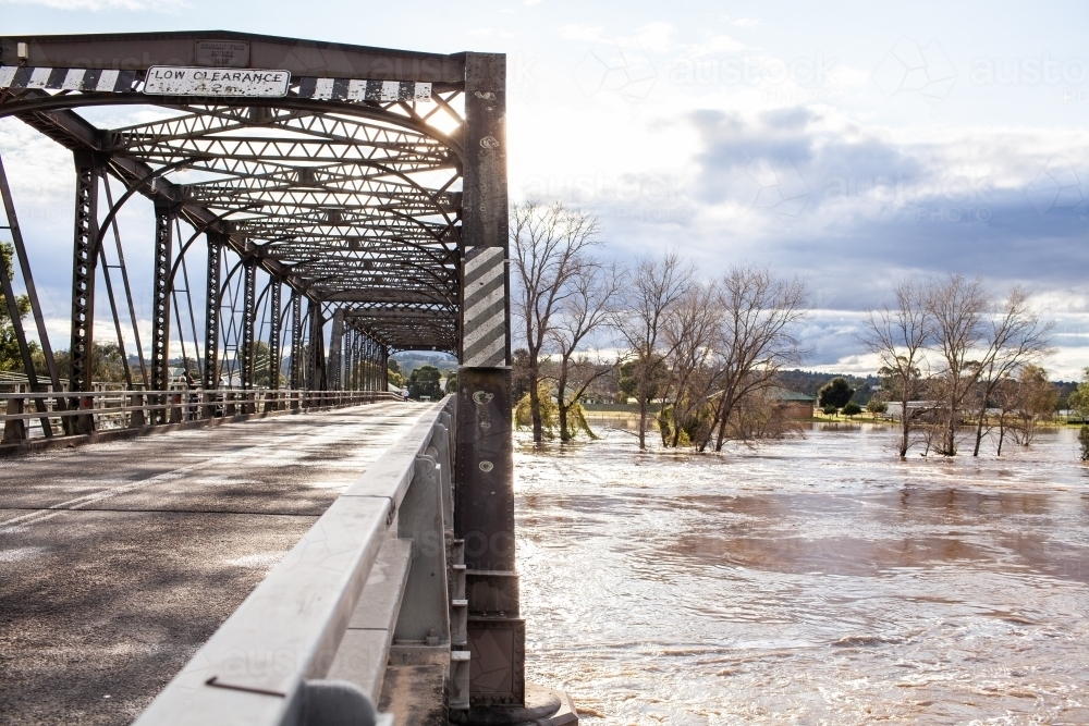 River with broken bank and floodwater over farmland beside bridge - Australian Stock Image