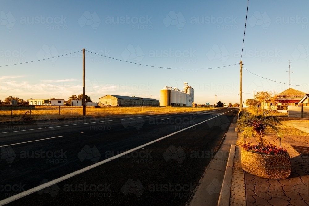 Road running through a country town with silos, blue sky and line markings - Australian Stock Image