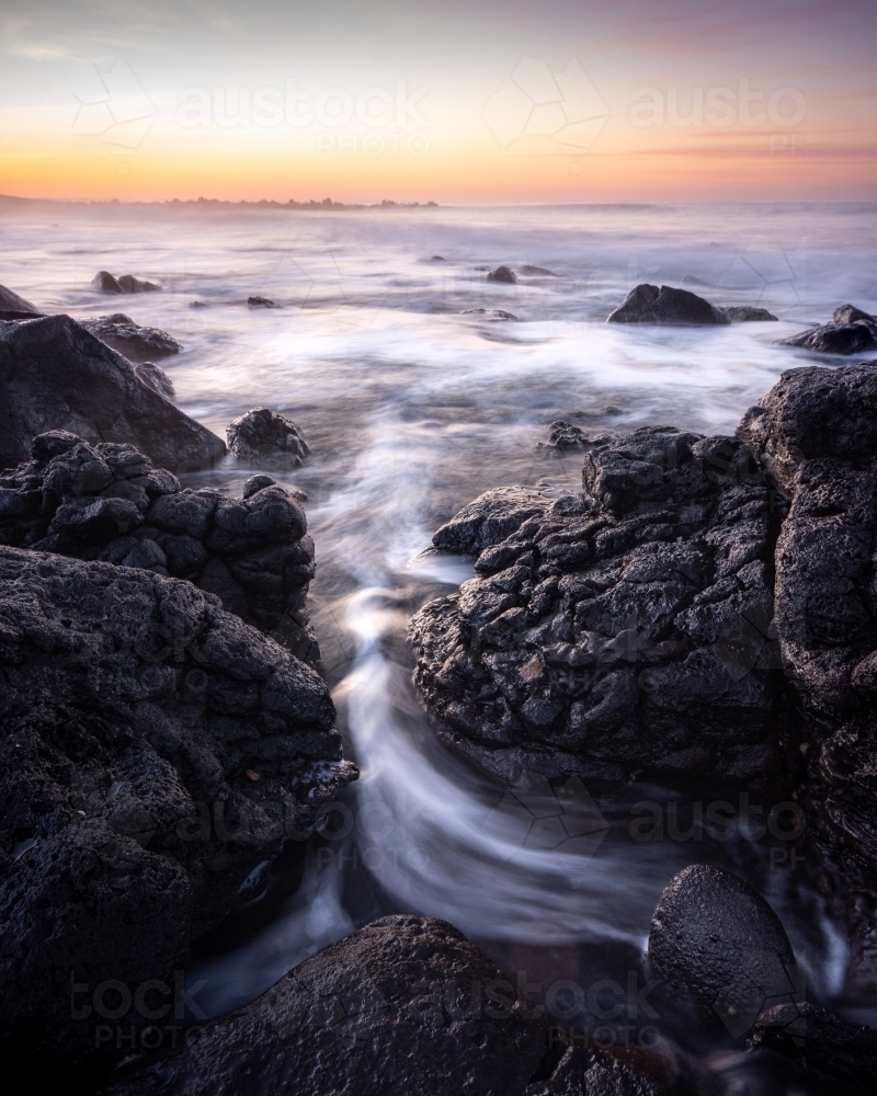 Rock formation with a stream of water towards the ocean - Australian Stock Image