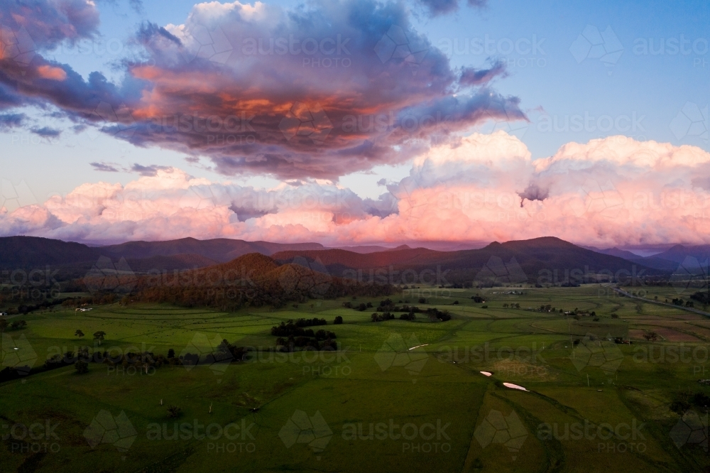 Rolling hills above green fields with pink clouds in sky - Australian Stock Image