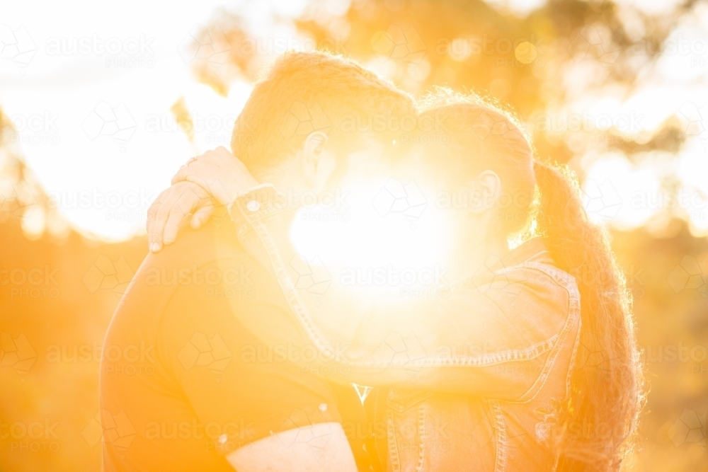 Romantic love shown with a hug in flare of golden light haze - Australian Stock Image