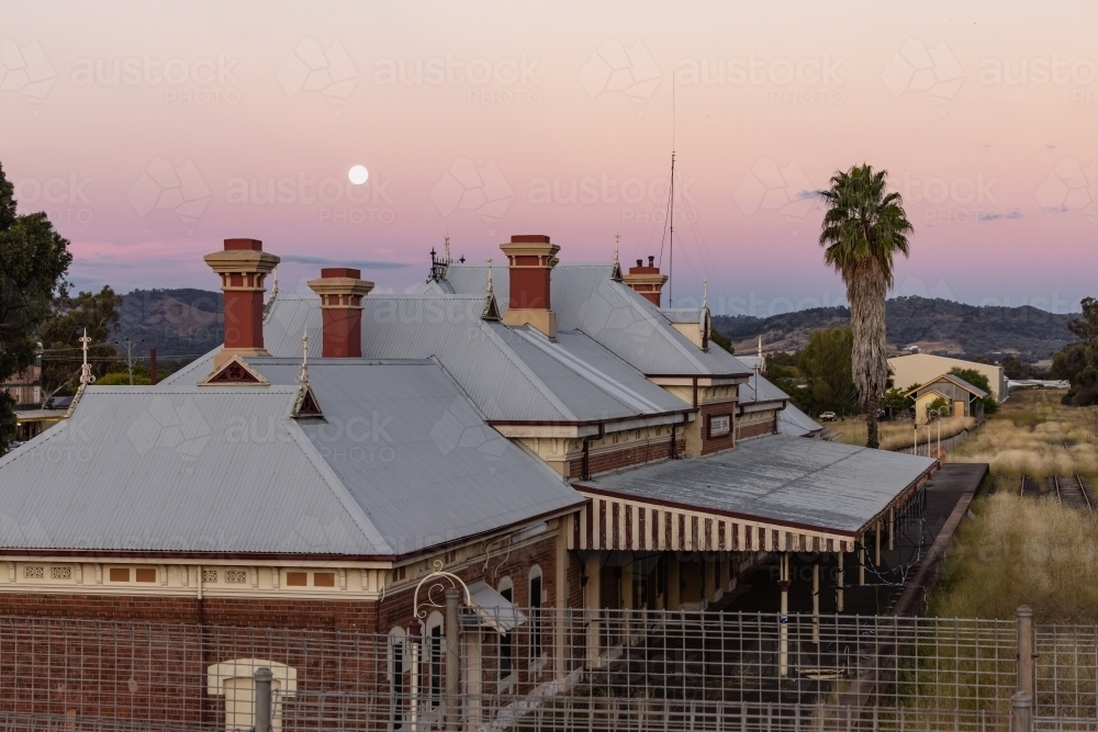 Rooftop of the historic Mudgee Railway Station with full moon in pink and purple twilight sky - Australian Stock Image