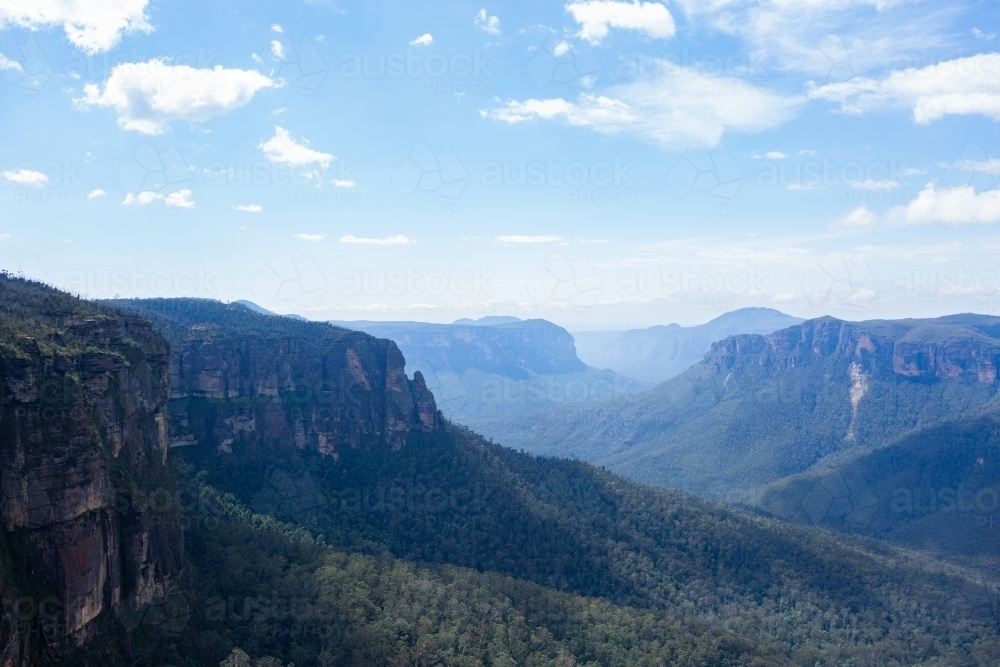 Rugged mountain ranges dip into tree filled valley seen from Govetts Leap - Australian Stock Image