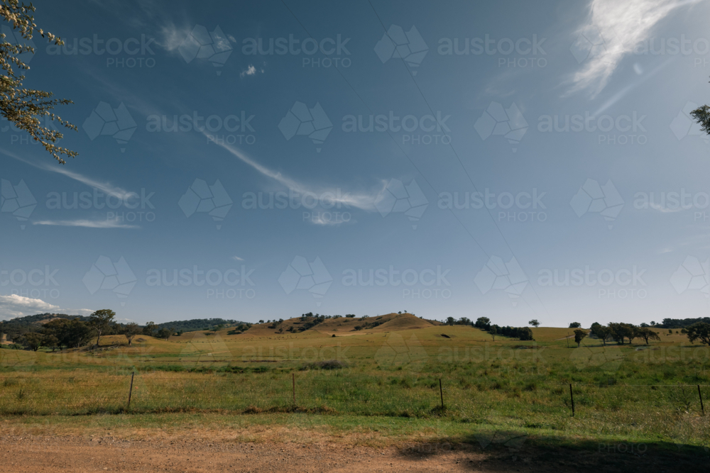 Rural landscape with rolling hills and trees under a clear sky - Australian Stock Image