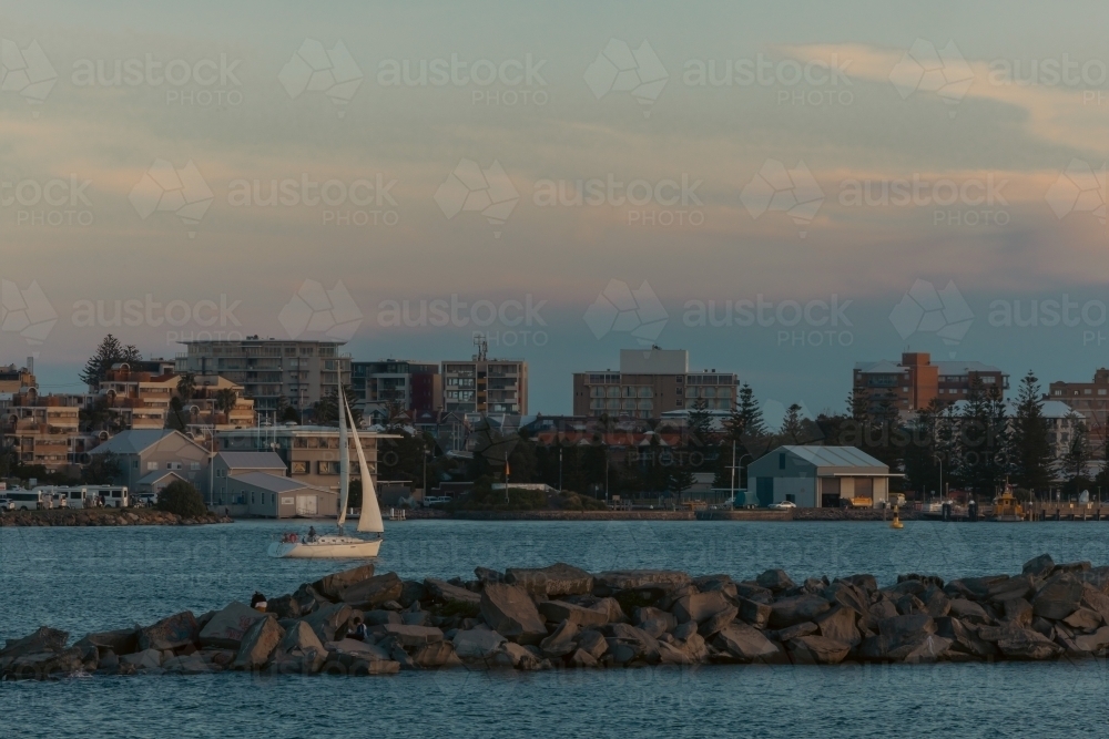 Sail boat entering the Hunter River past the Nobby's Beach breakwall at Newcastle, NSW - Australian Stock Image