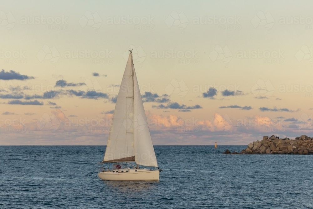Sail boat entering the Hunter River past the Nobby's Beach breakwall at Newcastle, NSW - Australian Stock Image