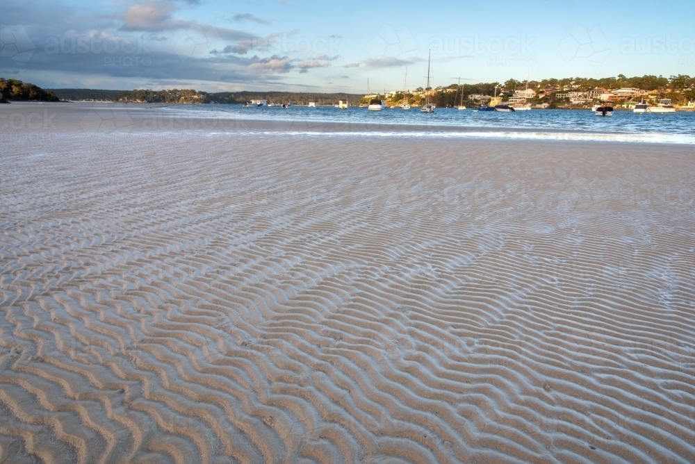 Sand flat with sinusoidal ripples in foreground and houses in the background - Australian Stock Image