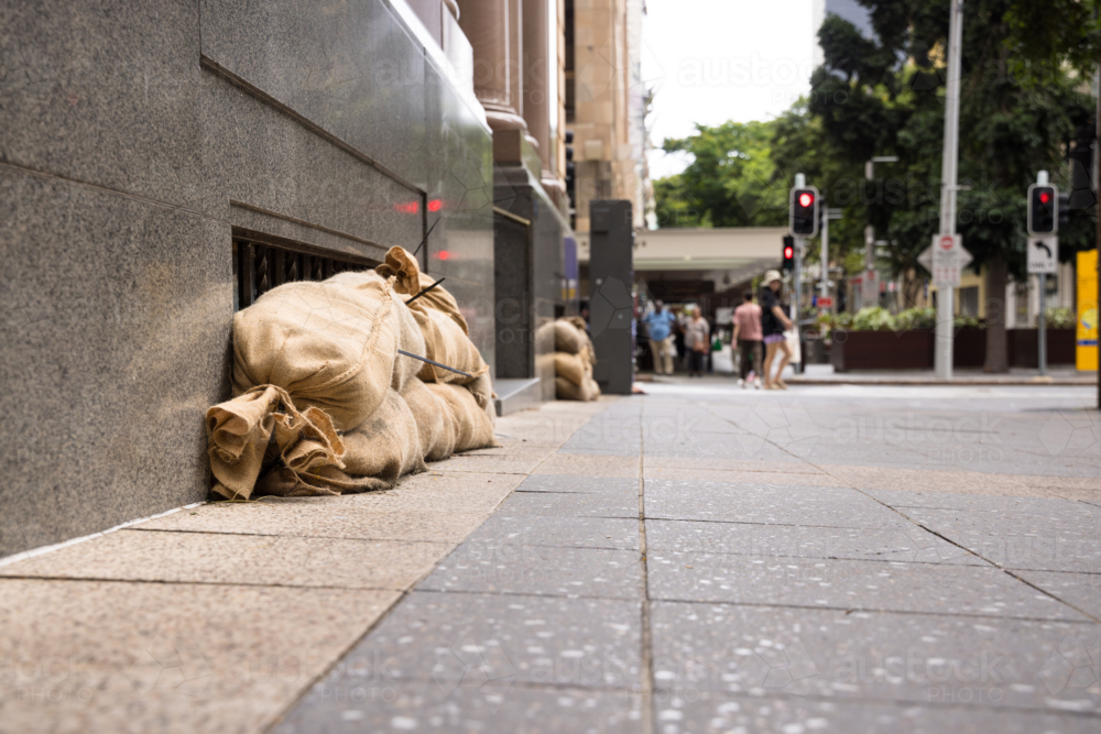 Sandbags along the footpath lining the lower windows of a building in Brisbane CBD before a cyclone - Australian Stock Image