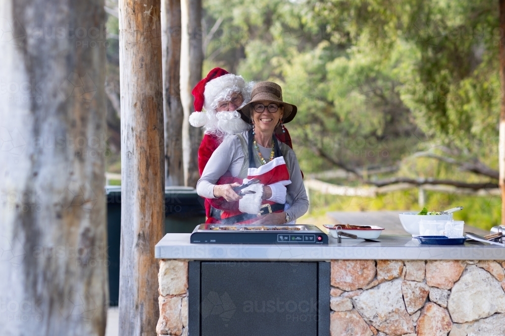 santa and mrs claus cooking a bbq in a park for a christmas meal - Australian Stock Image