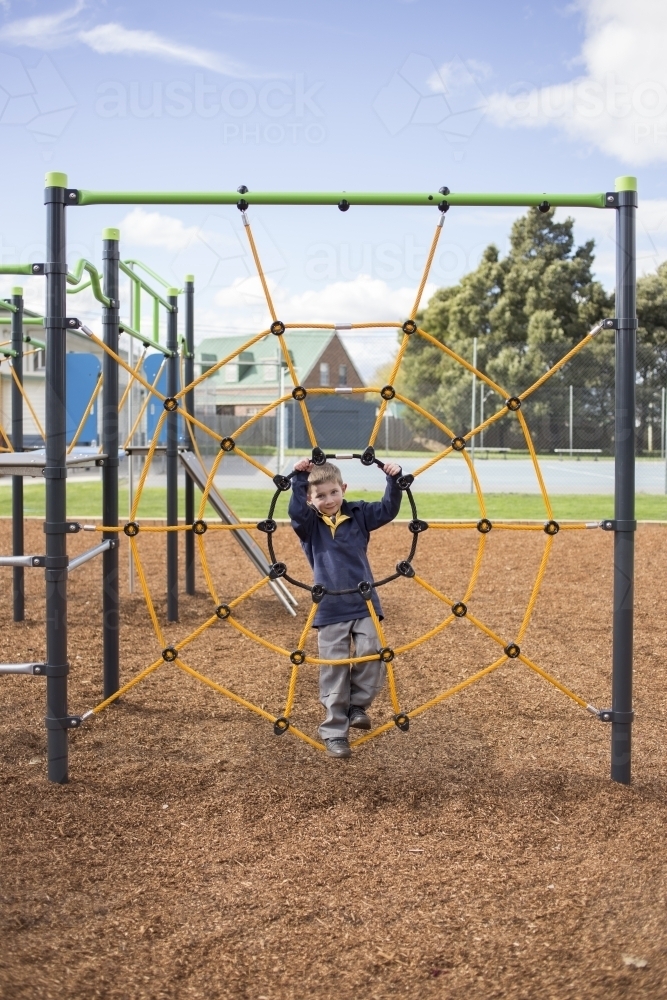 School age boy on climbing net at park - Australian Stock Image