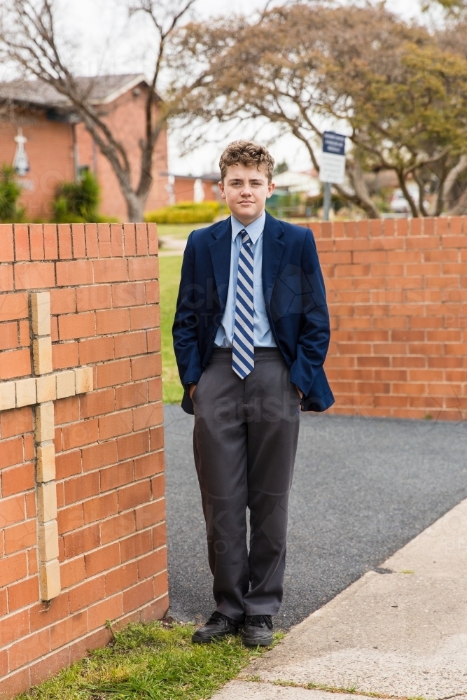 School boy in uniform standing with hands in pockets at entrance to private school with cross - Australian Stock Image