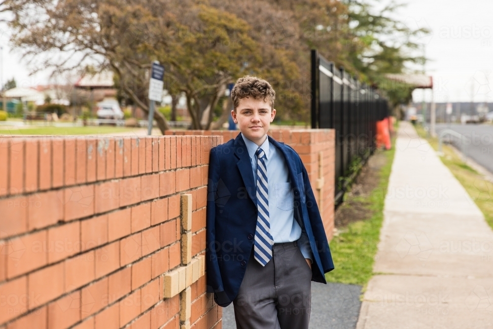 School boy leaning against brick entry with cross to private catholic school - Australian Stock Image