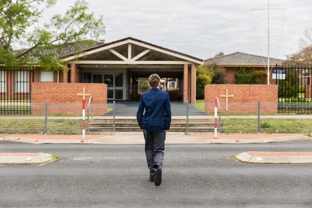 School boy walking across road to school wearing uniform - Australian Stock Image