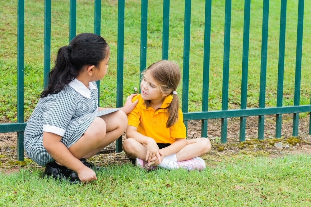 school kid comforting lonely younger girl in playground who got left out by friends - Australian Stock Image