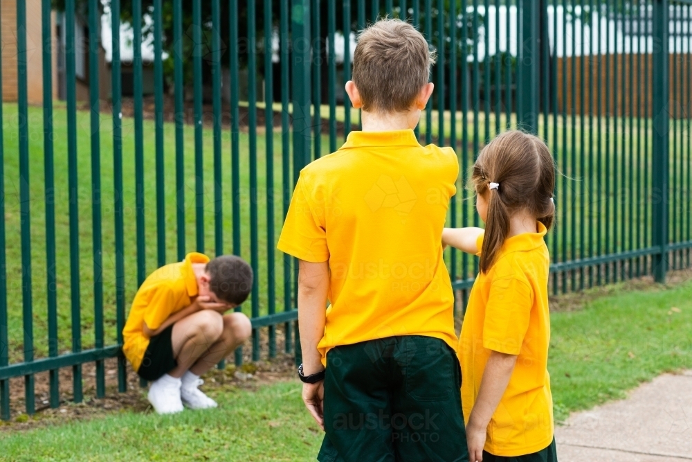 School kids bullying child hunched over by fence - Australian Stock Image