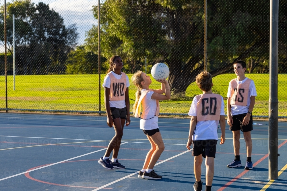 Image of schoolchildren on outdoor court practising netball with short ...