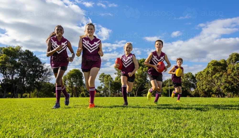 schoolchildren running towards camera in football uniforms on green grass - Australian Stock Image