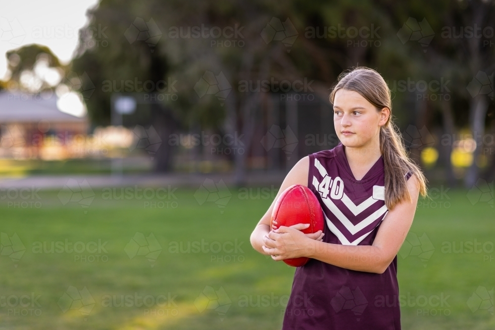 schoolgirl football player holding red leather football - Australian Stock Image