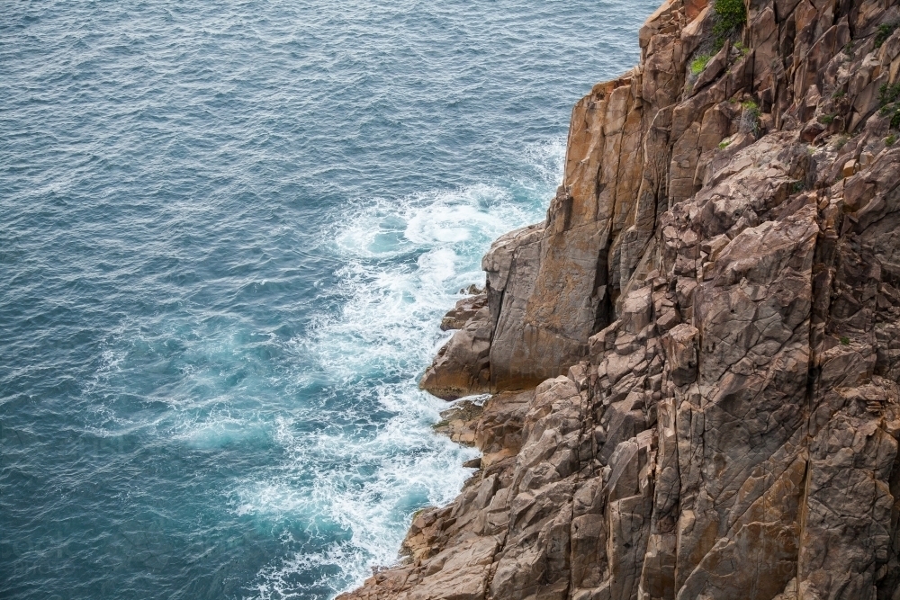 Sea waves crashing against brown rocks of a coastal cliff - Australian Stock Image