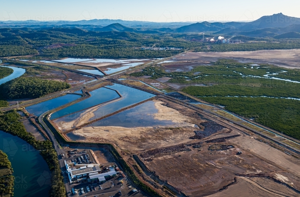 Sedimentation ponds at Wiggins Island Coal Export Terminal (Wicet) with industrial sites and hills. - Australian Stock Image