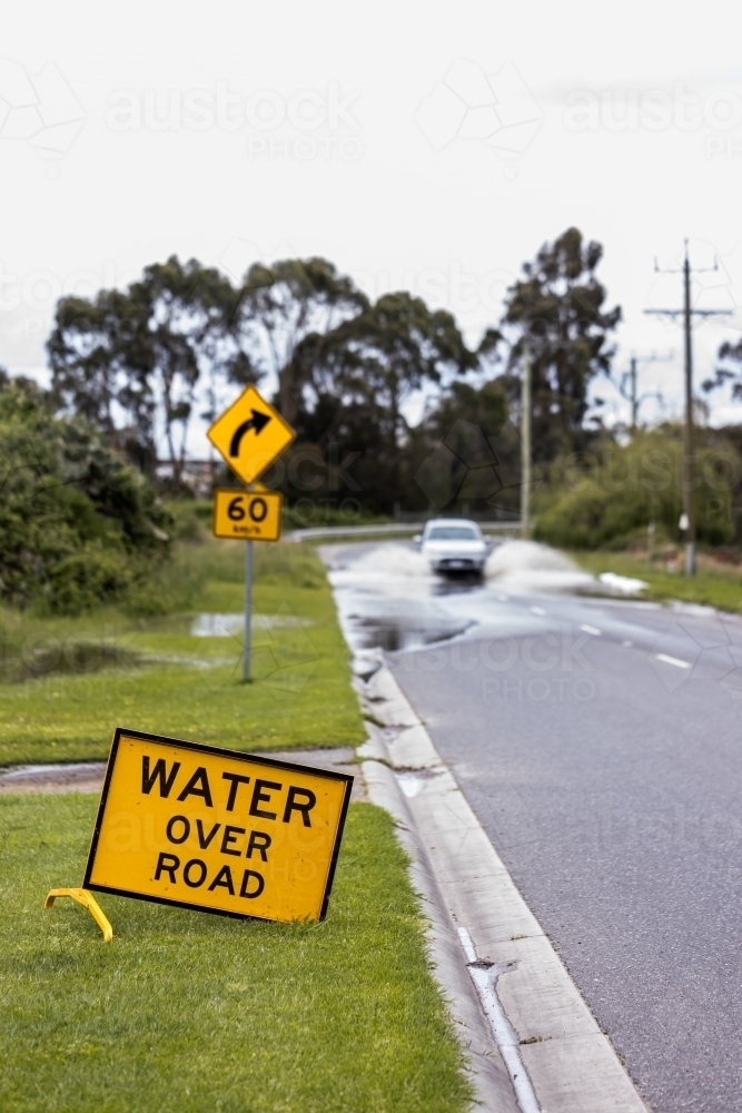 selective focus on a 'water over road' sign with an out of focus unrecognisable car in background - Australian Stock Image