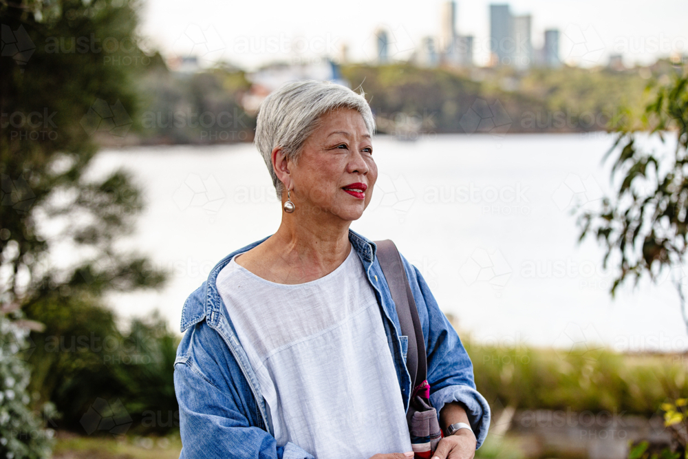 Senior Asian woman standing along the waterfront - Australian Stock Image