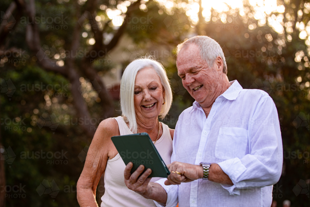 Senior couple holding and looking on a tablet outdoors - Australian Stock Image
