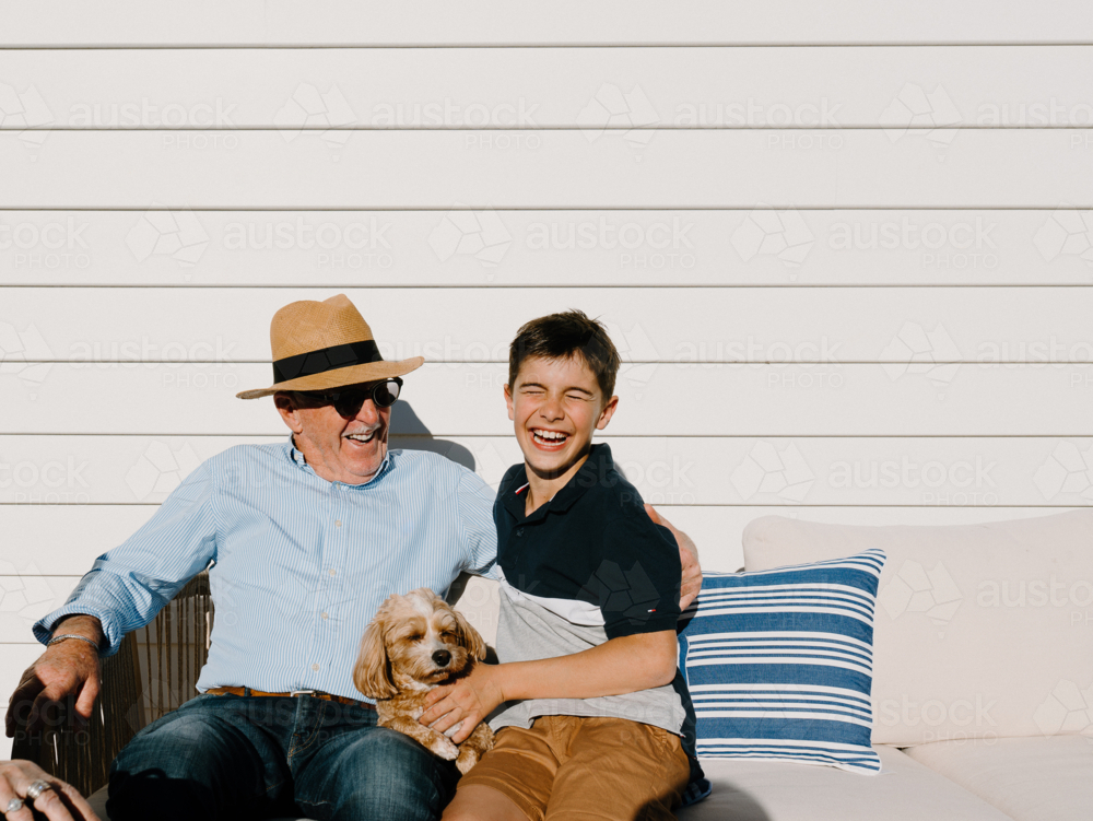 Senior man sitting with a young boy and small dog on the couch. - Australian Stock Image