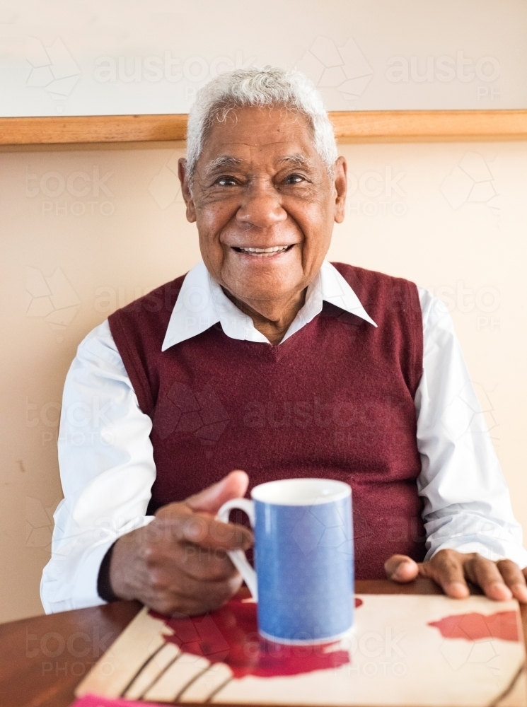 Senior man with Indonesian heritage smiles for the camera with a cup of coffee - Australian Stock Image