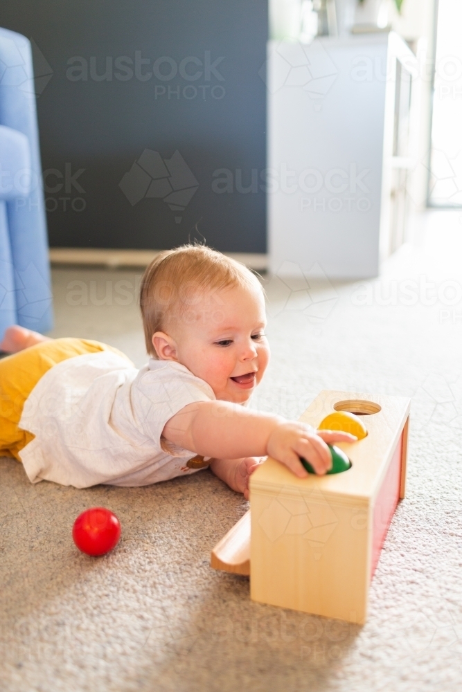 Seven month old baby playing with object permanence ball drop toy on floor - Australian Stock Image