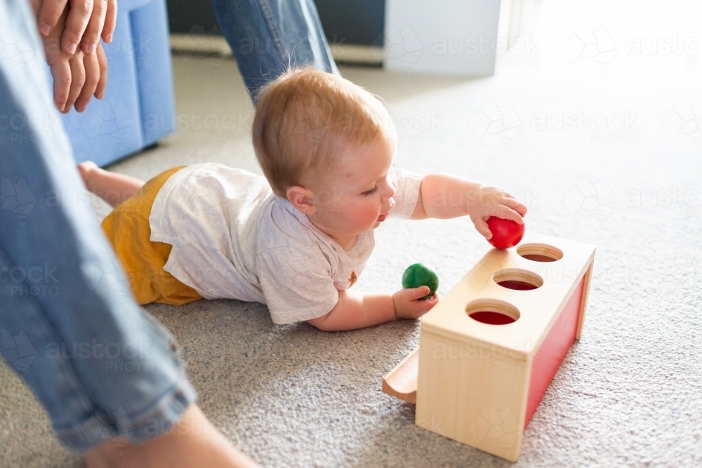 Seven month old baby playing with object permanence ball drop toy on floor - Australian Stock Image