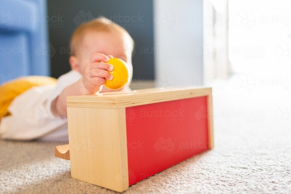 Seven month old baby playing with object permanence ball drop toy on floor - Australian Stock Image