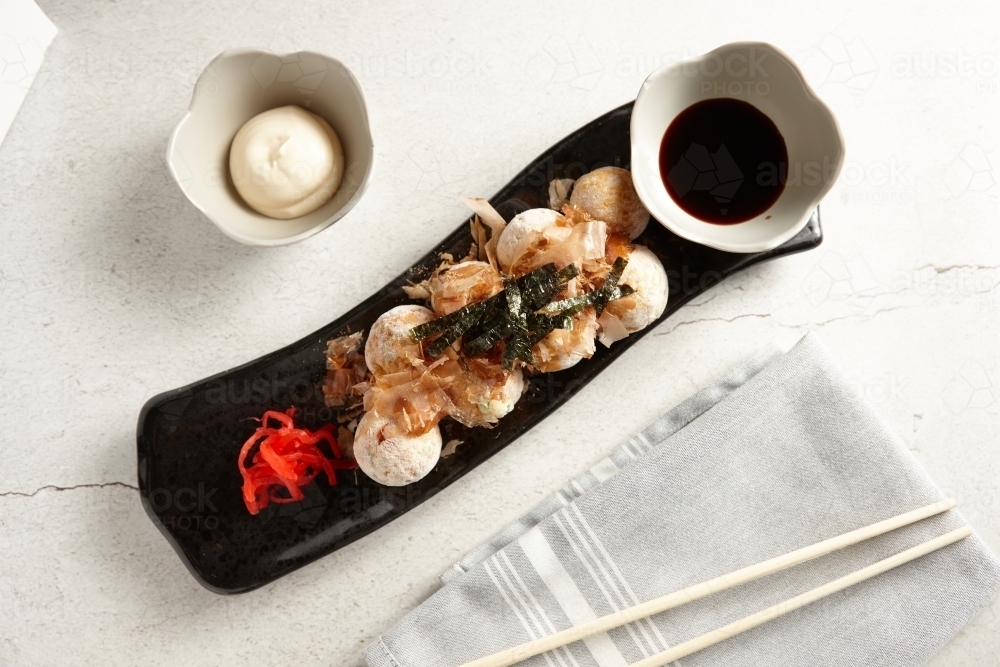 seven pieces of takoyaki with soy sauce and mayonnaise and chopsticks on the side - Australian Stock Image