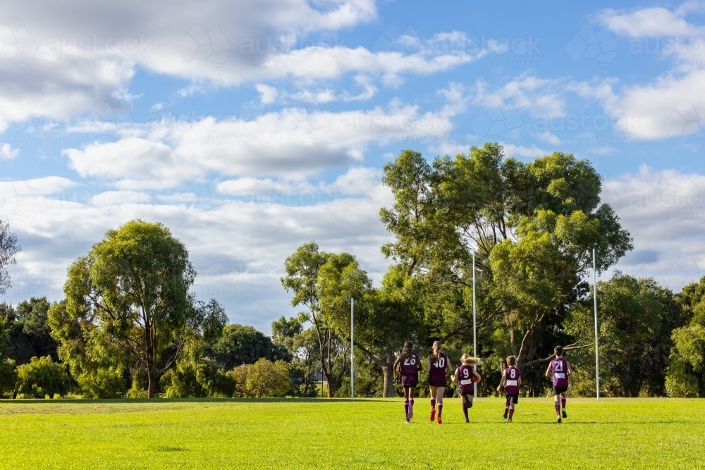 several kids in footy uniforms running towards goalposts on football field - Australian Stock Image