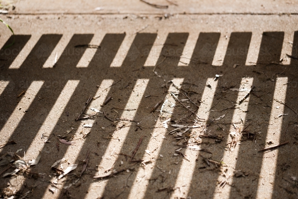 shadow of a paling gate on a path strewn with leaves and twigs - Australian Stock Image