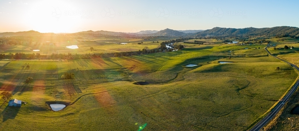 Shed and dams on green Australian farmland with golden sunset light over landscape - Australian Stock Image