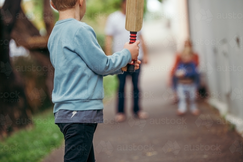 Image of Shot from behind of young boy playing cricket in the street ...