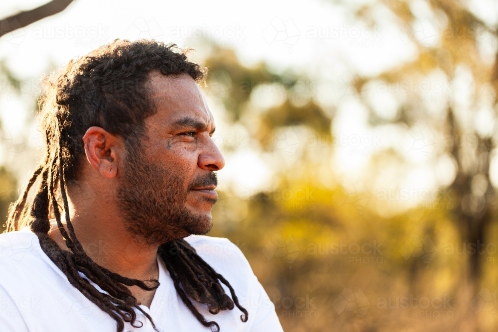 Side profile portrait of aboriginal man looking away with dreadlocks and neutral expression - Australian Stock Image