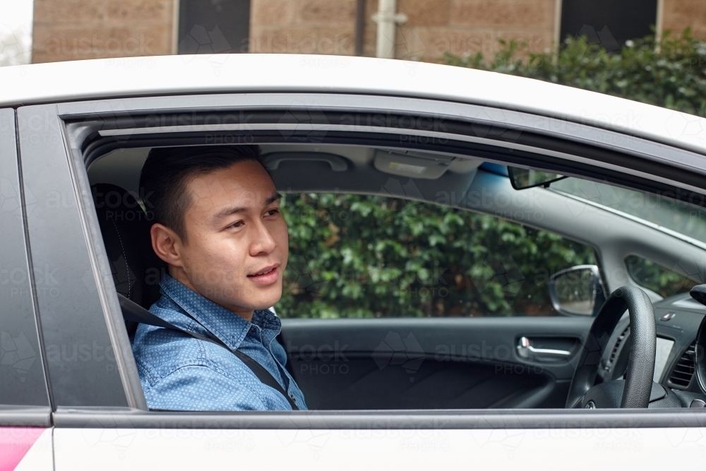 Side view of Asian man driving in car looking out window - Australian Stock Image