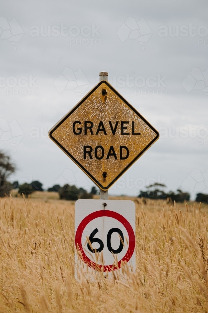 Sign with 'GRAVEL ROAD' and '60' in field with long grass - Australian Stock Image