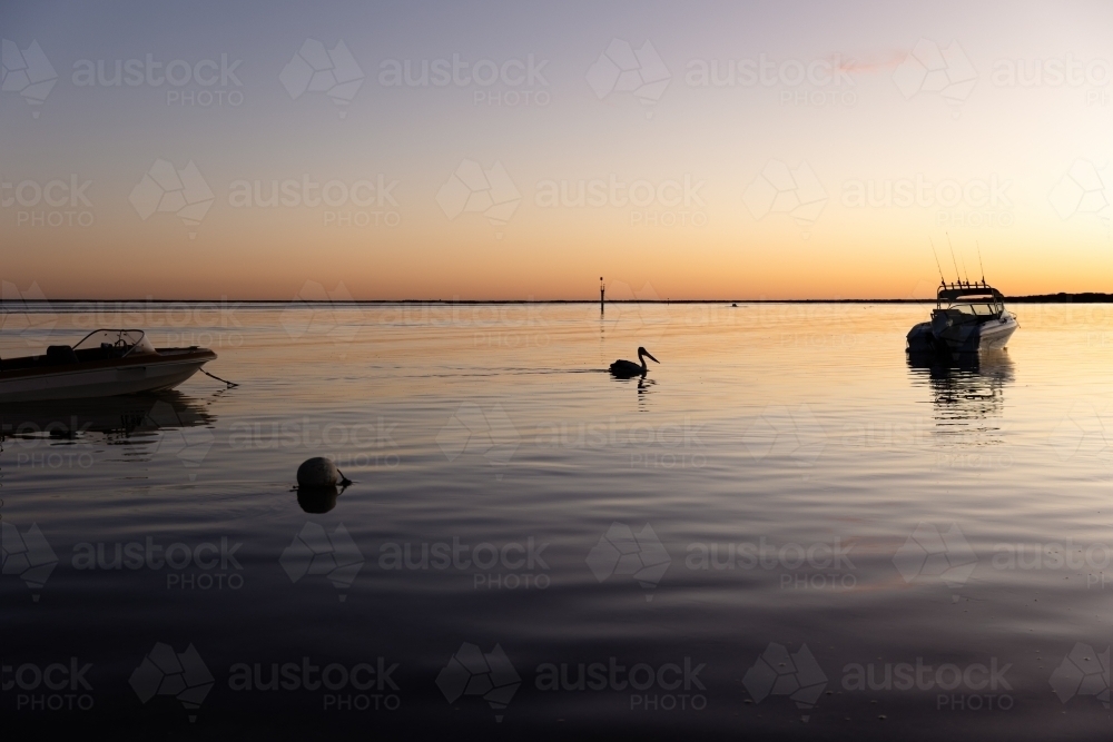 Silhouette of buoy, pelican and boats on bay in evening - Australian Stock Image