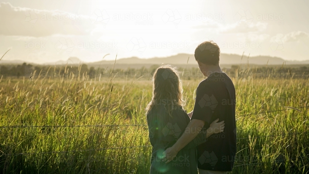 Silhouette of couple standing in field watching sunset - Australian Stock Image