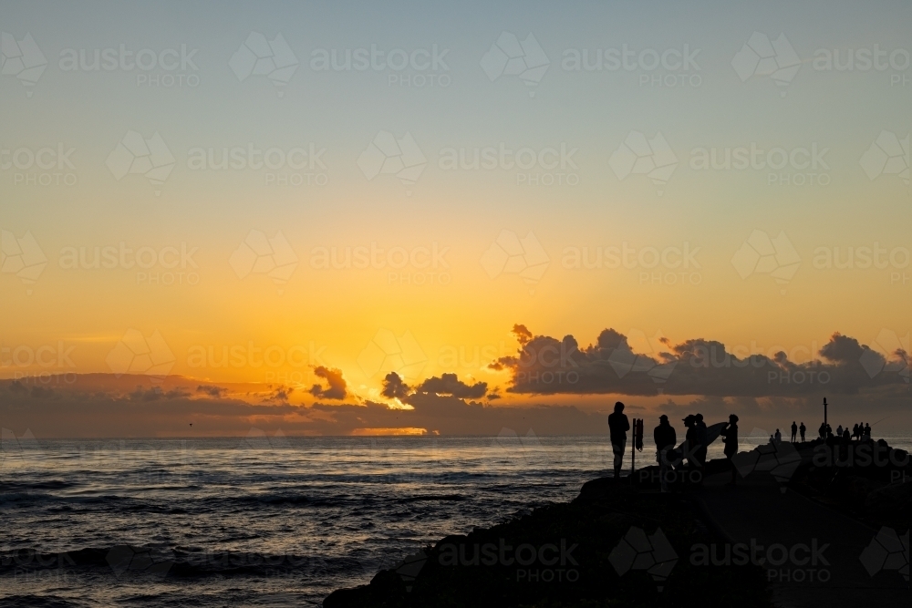 Silhouette of group of people gathering to watch the sunrise from the breakwall at Brunswick Heads - Australian Stock Image