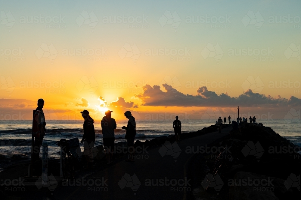 Silhouette of group of people gathering to watch the sunrise from the breakwall at Brunswick Heads - Australian Stock Image