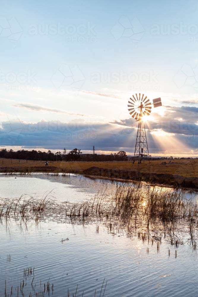 Silhouette of windmill and sunlight and farm dam at sunset - Australian Stock Image