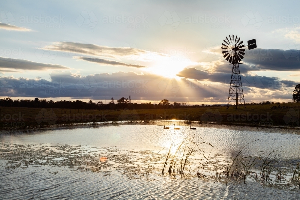 Silhouette of windmill and sunlight and farm dam at sunset - Australian Stock Image