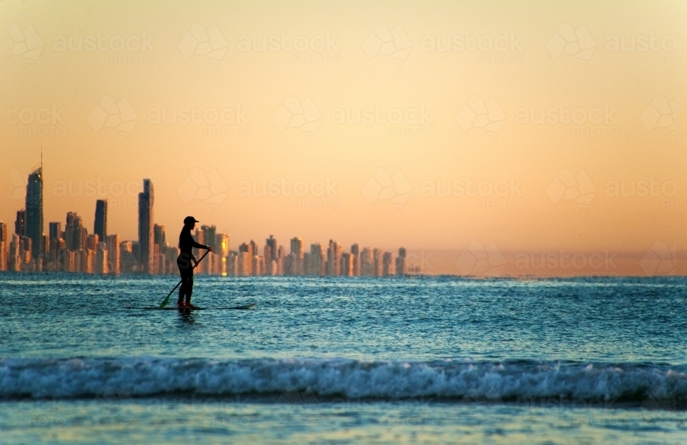 Silhouette of woman on stand up paddler against Gold Coast skyline. - Australian Stock Image