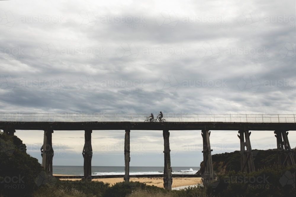 silhouette photos of bicycle riders on Kilcunda Bourne Creek Trestle Bridge on an overcast day - Australian Stock Image