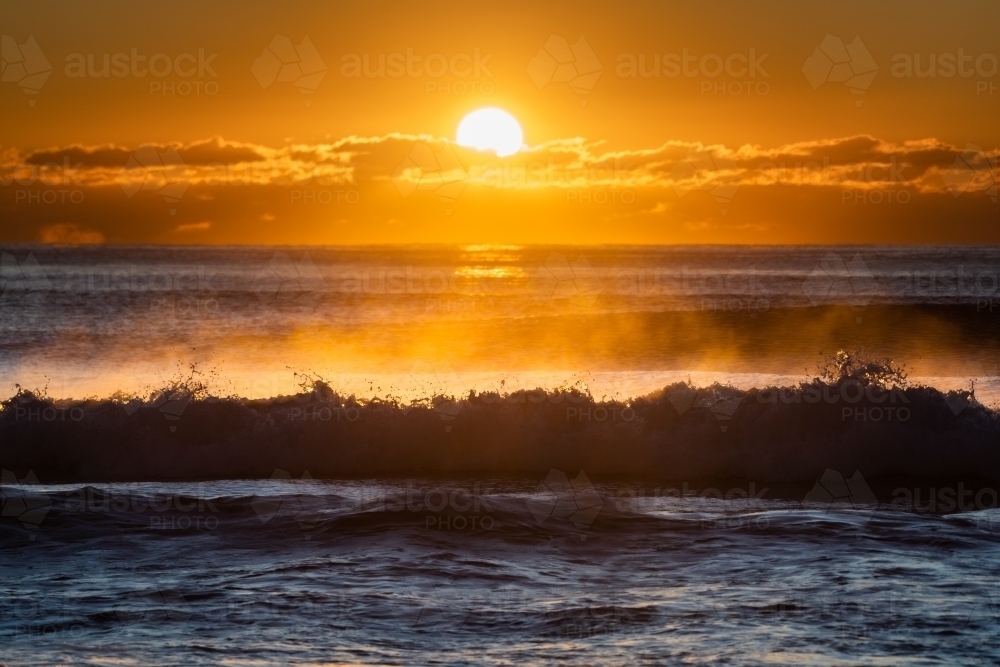 silhouette shot of big waves in the ocean at sunrise - Australian Stock Image